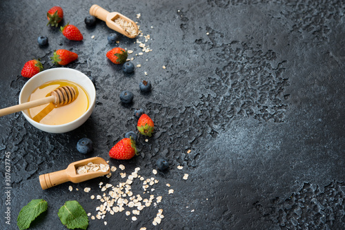 The ingredients for a healthy and balanced Breakfast are laid out on a concrete background with the help of space. Oatmeal, berries and honey.