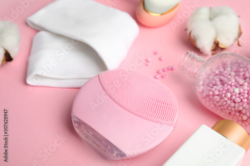 Face cleansing brush and cosmetic products on pink background