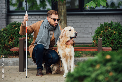Blind man with walking stick hugging guide dog on street photo