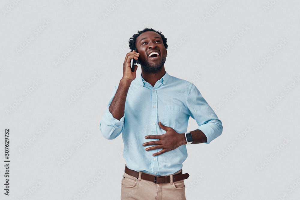 Handsome young African man talking on the phone and smiling while standing against grey background Handsome young African man talking on the phone and smiling while standing against grey background