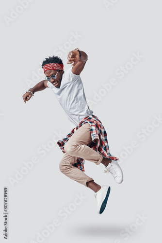 Full length of playful young African man smiling while hovering against grey background