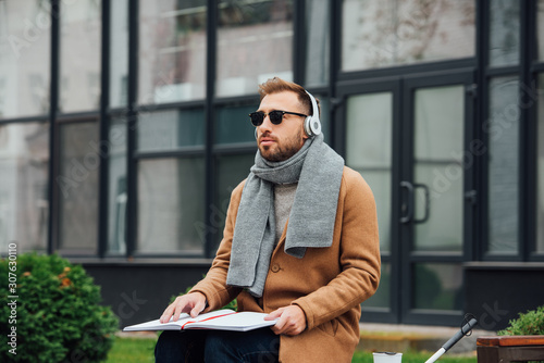 Blind man in headphones reading book on bench in park photo