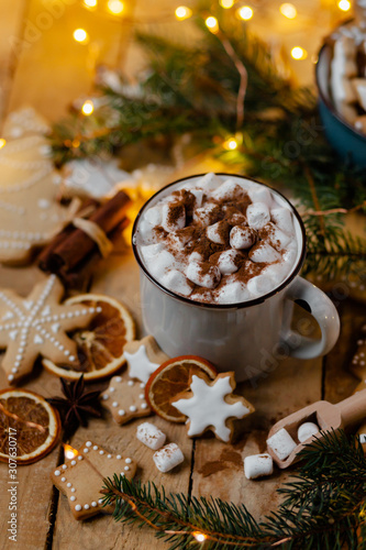 Winter hot drink: white mug with hot chocolate with marshmallow and cinnamon. Cozy home atmosphere, festive holiday mood. Rustic style, wooden background. Homemade gingerbread cookies