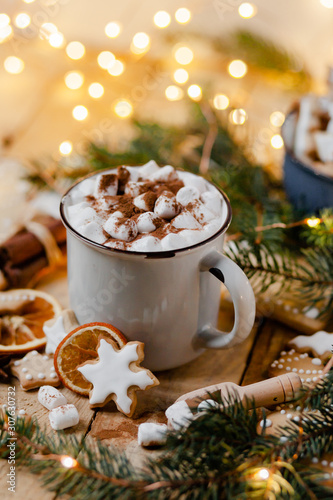 Winter hot drink: white mug with hot chocolate with marshmallow and cinnamon. Cozy home atmosphere, festive holiday mood. Rustic style, wooden background. Homemade gingerbread cookies