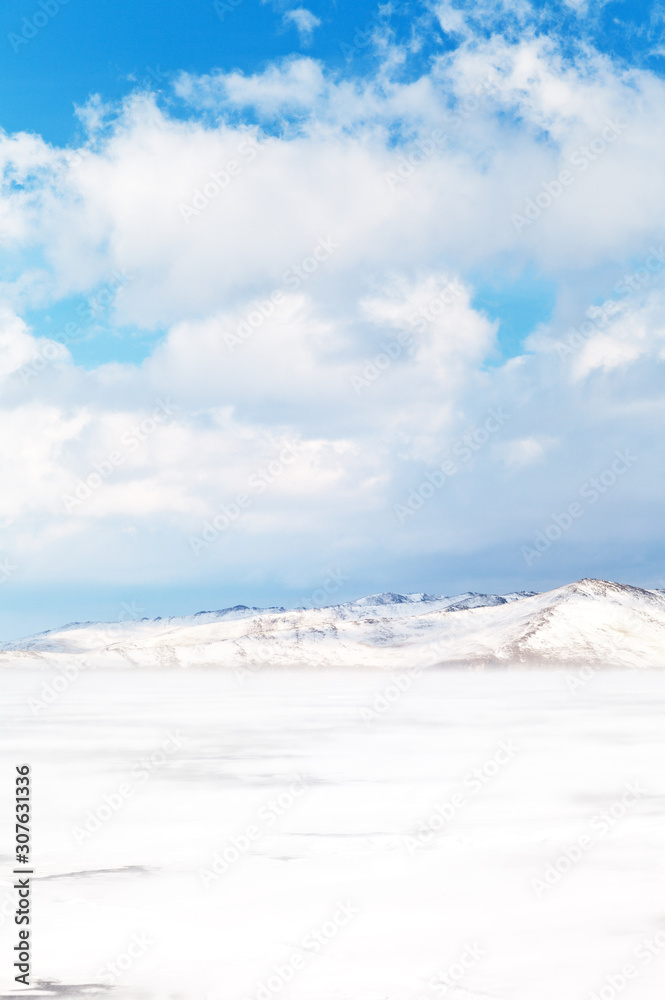 Beautiful winter landscape of frozen Lake Baikal with snowy white hills of Olkhon Island on a February day. Cold light natural background