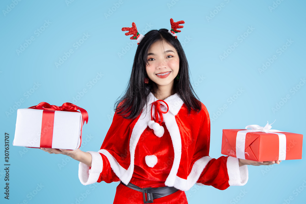 Happy Asian in Santa Claus costume holding Christmas  gift box on blue background.