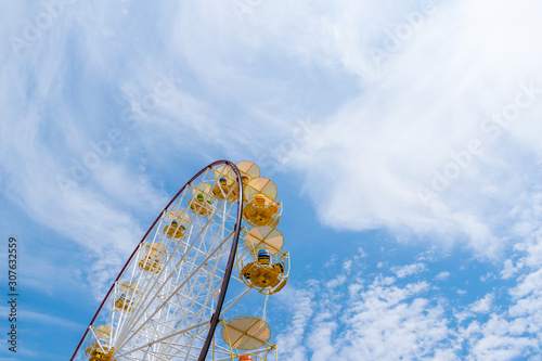 Ferris wheel on a natural blue and cloudy sky background. Yellow cabins with four seats.