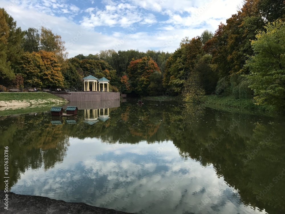 View from the bridge to the autumn Park and two rotunda on the other side under the blue and white clouds sky. View from the bridge to the autumn Park and two rotunda on the other side under the blue and white clouds sky.