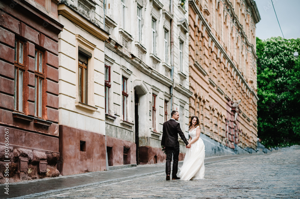 Portrait the groom and the bride going back near old building, old house outside, outdoor. Newlyweds are walking along the streets of the city of Lviv. Portrait the groom and the bride going back near old building, old house outside, outdoor. Newlyweds are walking along the streets of the city of Lviv.