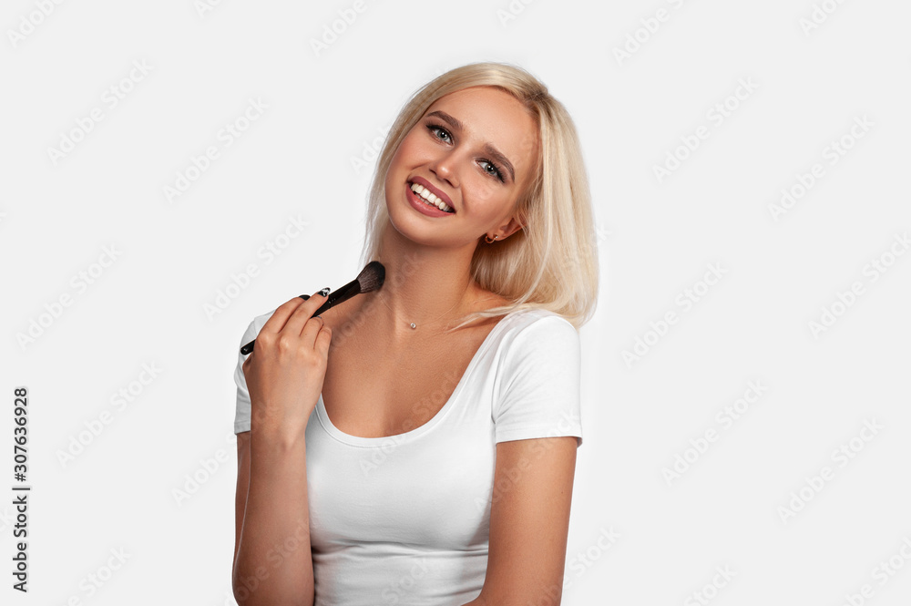 Beautiful blonde girl applies skin tone with Brush. Sexy woman portrait isolated on white background. Perfect Makeup. Skincare Foundation. Pretty girl with perfect skin smiling. Brushes Makeup Artist. Beautiful blonde girl applies skin tone with Brush. Sexy woman portrait isolated on white background. Perfect Makeup. Skincare Foundation. Pretty girl with perfect skin smiling. Brushes Makeup Artist.