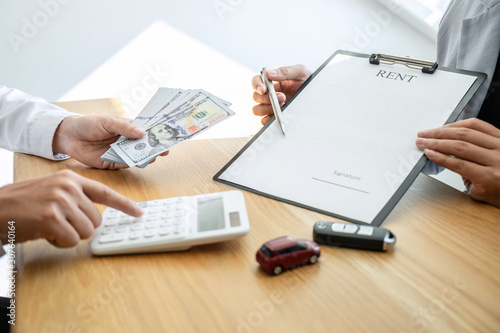 Car rental and Insurance concept, Young salesman receiving money and giving car's key to customer after sign agreement contract with approved good deal for rent or purchase