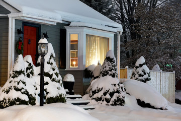 Real Christmas trees festively decorated with New Year and Christmas garlands and toys on the threshold of a simple house on a snowy winter evening. USA. Maine