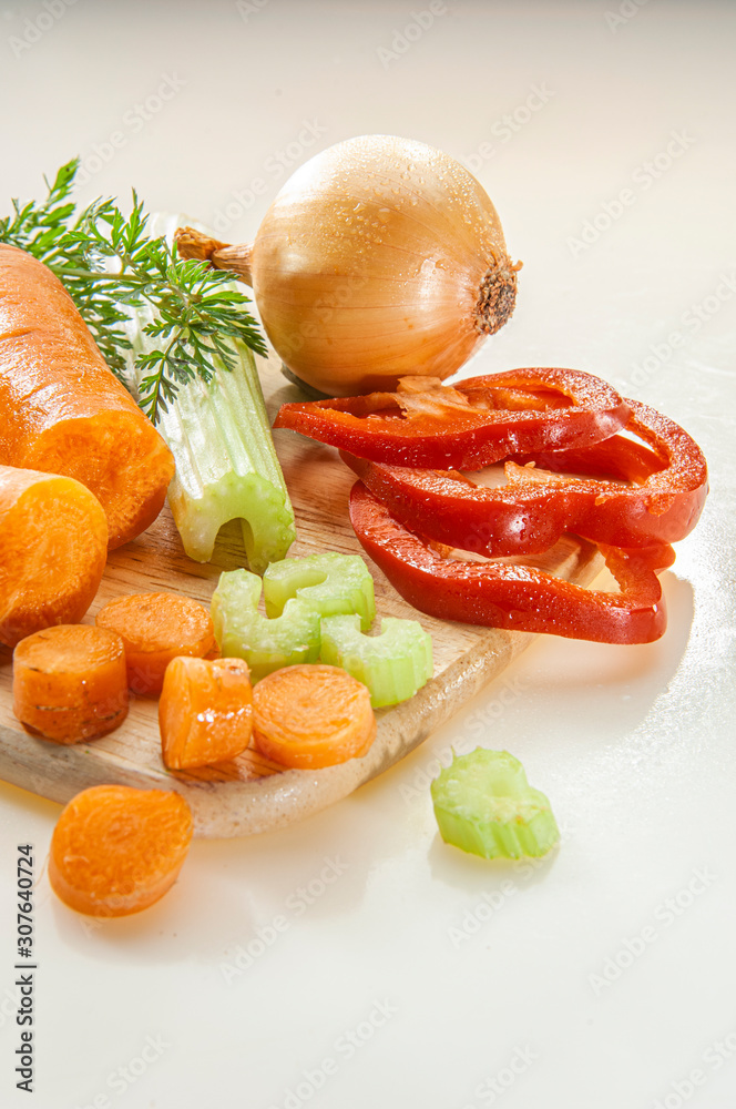 Karotten, Sellerie,m Zwiebel und Paprika auf einem Küchenbrett in Scheiben und Streifen geschnitten auf hellem Grund Karotten, Sellerie,m Zwiebel und Paprika auf einem Küchenbrett in Scheiben und Streifen geschnitten auf hellem Grund