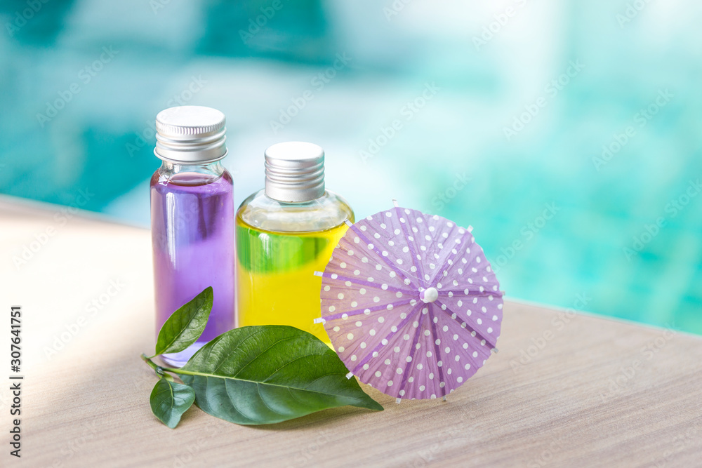 Yellow and purple gel in glass bottle with green leaf and paper umbrella over blurred blue water background, herble product concept