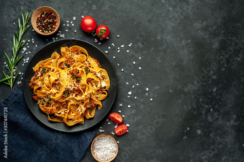 Pasta Bolognese with spices, Italian pasta dish with minced meat and tomatoes in a dark plate on a stone background with copy space for your text photo