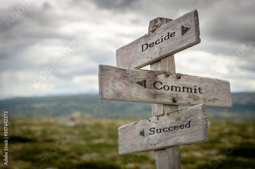 Decide commit and succeed text on wooden rustic signpost outdoors in nature/mountain scenery. Lifestyle, goals and hard work concept. photo