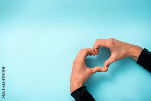 Fotografi cropped view of woman showing heart-shaped sign with hands on blue