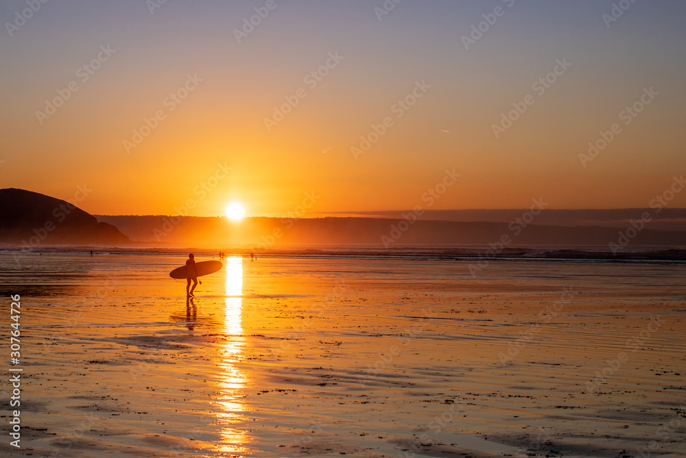 A surfer makes his way down the beach to the waves at sunset on Westward Ho! Beach A surfer makes his way down the beach to the waves at sunset on Westward Ho! Beach