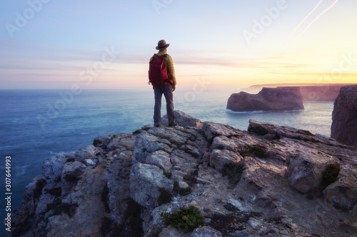 A rear view of of a lone male backpacker or hiker standing on a cliff top with a Fototapeta
