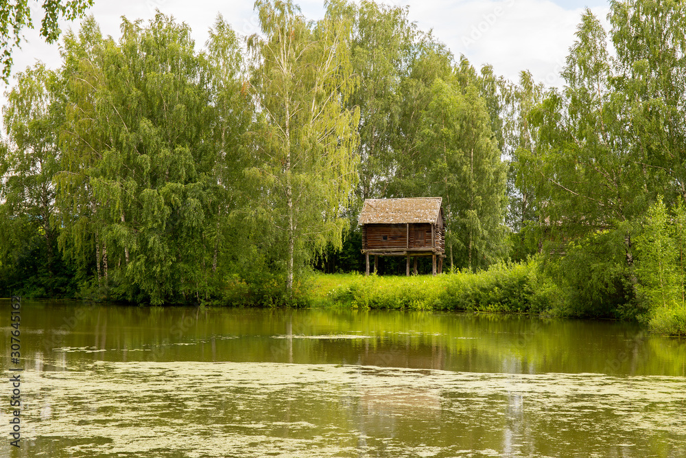 Obraz premium Rural landscape. Sheds for storage of agricultural goods are located on the river Bank among the birches. Kostroma, Russia.