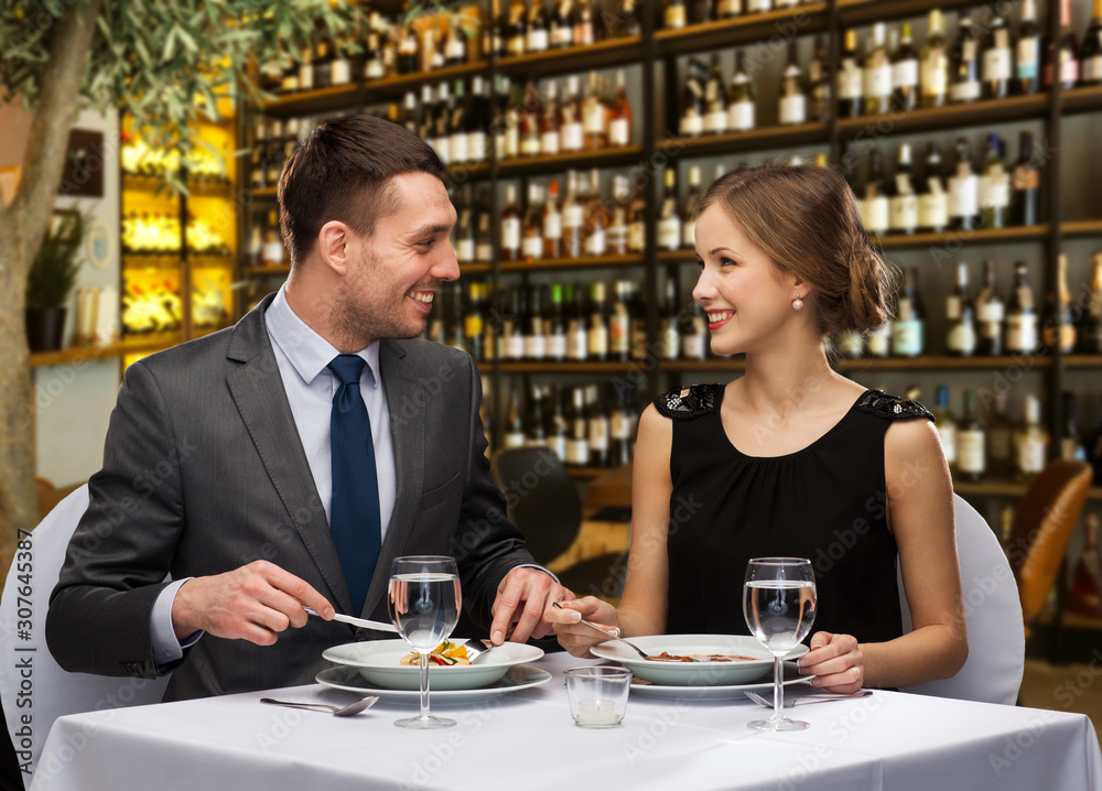 leisure and luxury concept - smiling couple eating main course over restaurant or wine bar background