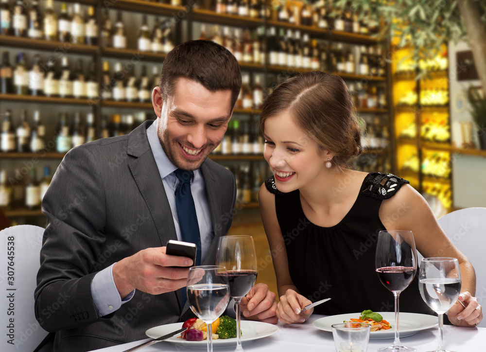leisure and luxury concept - smiling couple with smartphone and food over restaurant or wine bar background