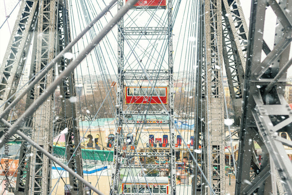 aerial red cabin view and steel frame construction of oldest ferris wheel in Vienna Prater amusement fair park during cold snowy winter day. Snowfall blizzard weather in european city