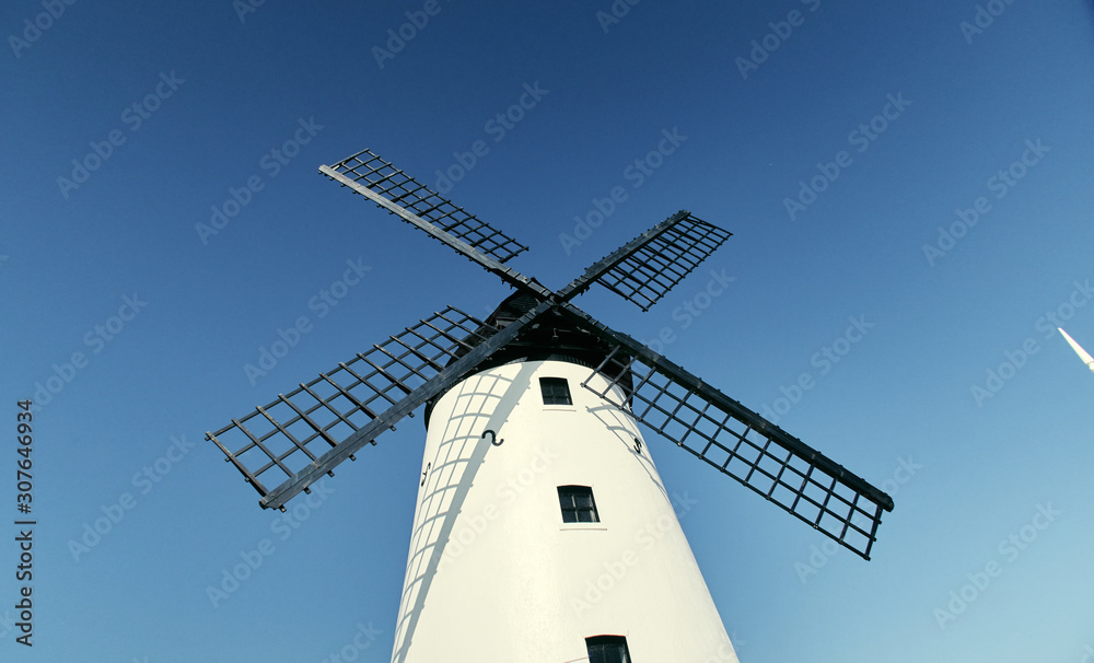 A vintage dutch style windmill against a beautiful blue clear sky. Windmills produce a clean way of harnessing the earths natural power resource of wind. Clean energy in farming and food production.