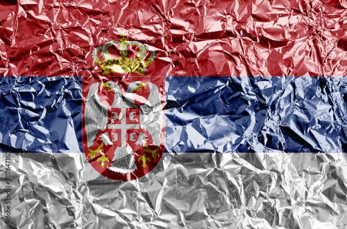 Serbia flag depicted in paint colors on shiny crumpled aluminium foil closeup. Textured banner on rough background photo