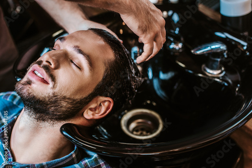 barber washing hair of bearded man in black sink