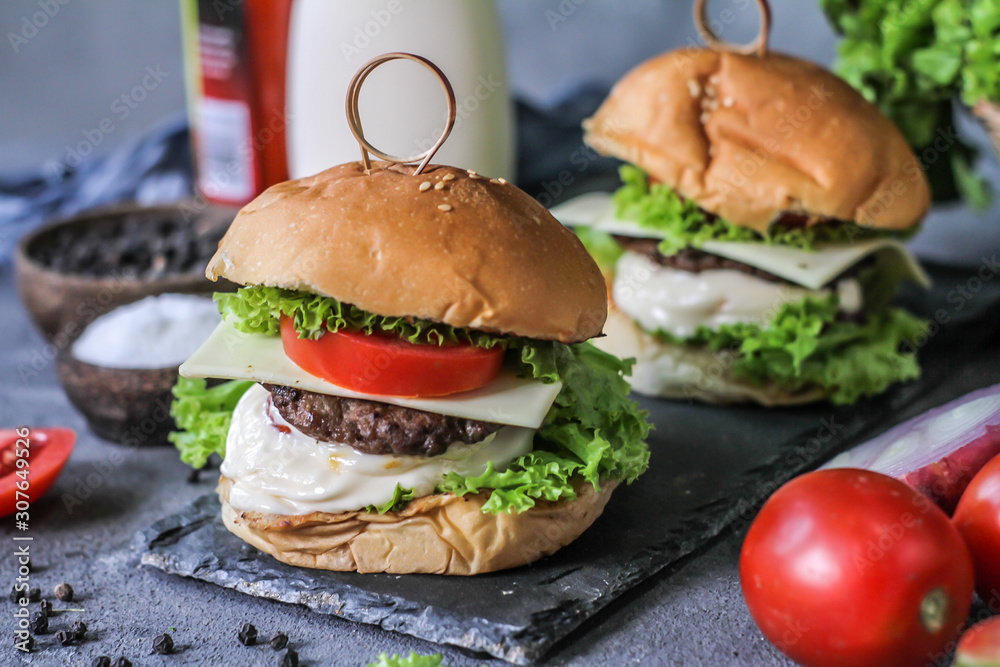 Photo of fresh burger on wooden cutting board on dark background..Homemade hamburger with beef, onion, tomato, lettuce and cheese. Homemade fast food. Dark textured background. Copy space. Image. Photo of fresh burger on wooden cutting board on dark background..Homemade hamburger with beef, onion, tomato, lettuce and cheese. Homemade fast food. Dark textured background. Copy space. Image.