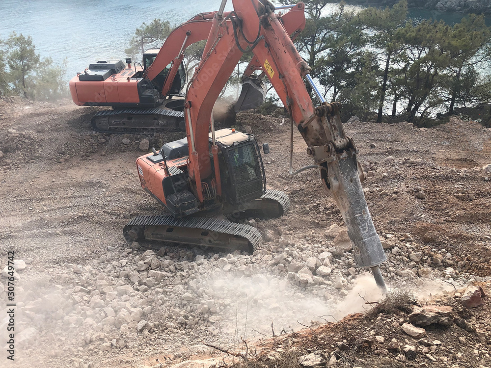 Fototapeta premium Hydrohammer is crushing rocks during road construction works on the rocky soils. Heavy machinery at earthmoving