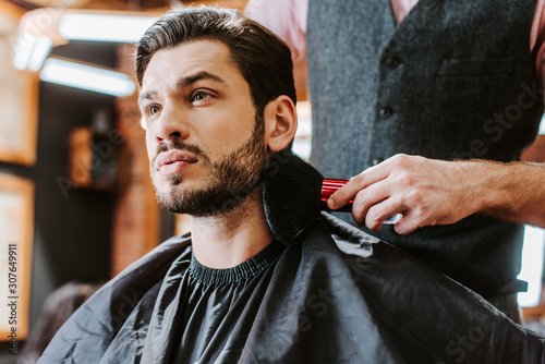 selective focus of barber holding cosmetic brush near face of bearded man