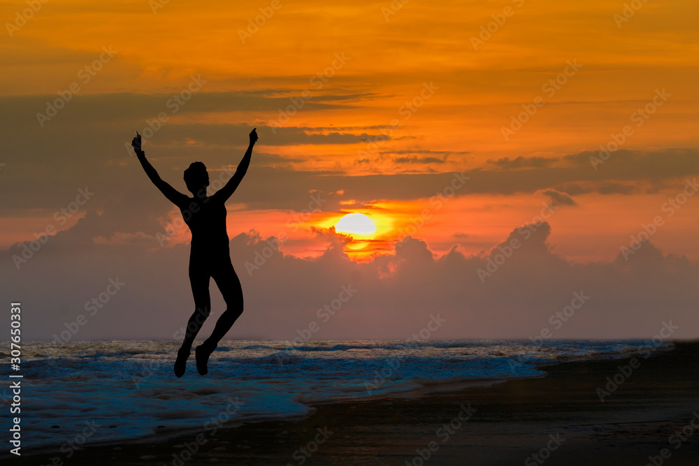Happy sport woman silhouette jumping for joy on the beach at big sunset. Success, winner, happiness