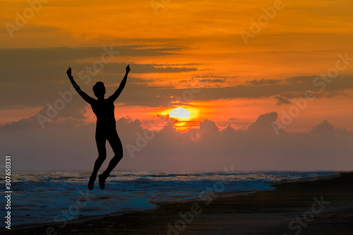 Happy sport woman silhouette jumping for joy on the beach at big sunset. Success  winner  happiness