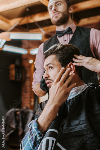 selective focus of handsome man touching hair near barber