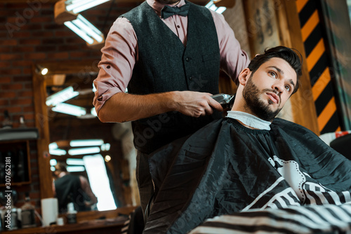 stylish barber holding trimmer while styling hair of man