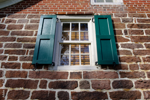 Stone wall exterior with window and green shutters. 