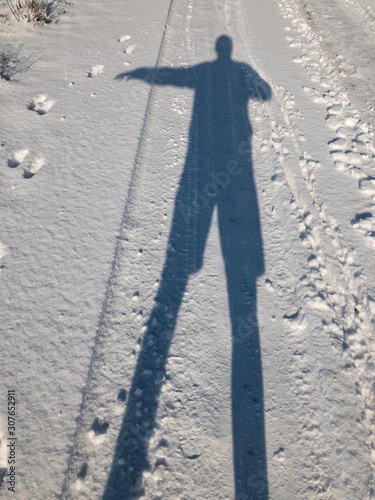 Silhouette of a man doing stop sign while standing on an earth road covered with fresh snow
