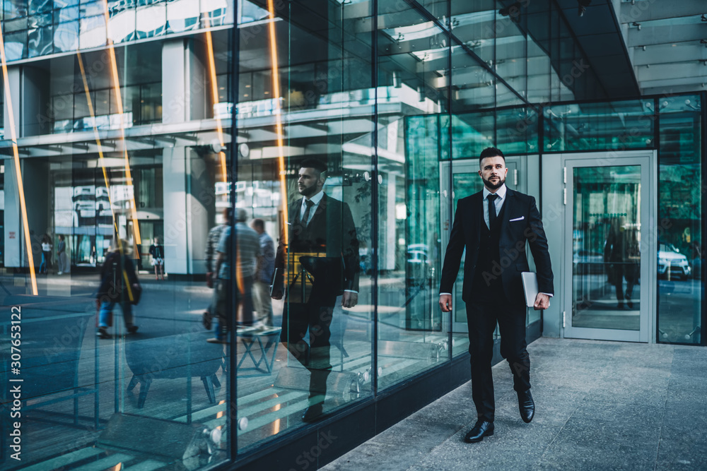 Confident manager with tablet walking near glass wall