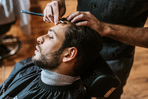 barber holding sharp razor while doing haircut to handsome man
