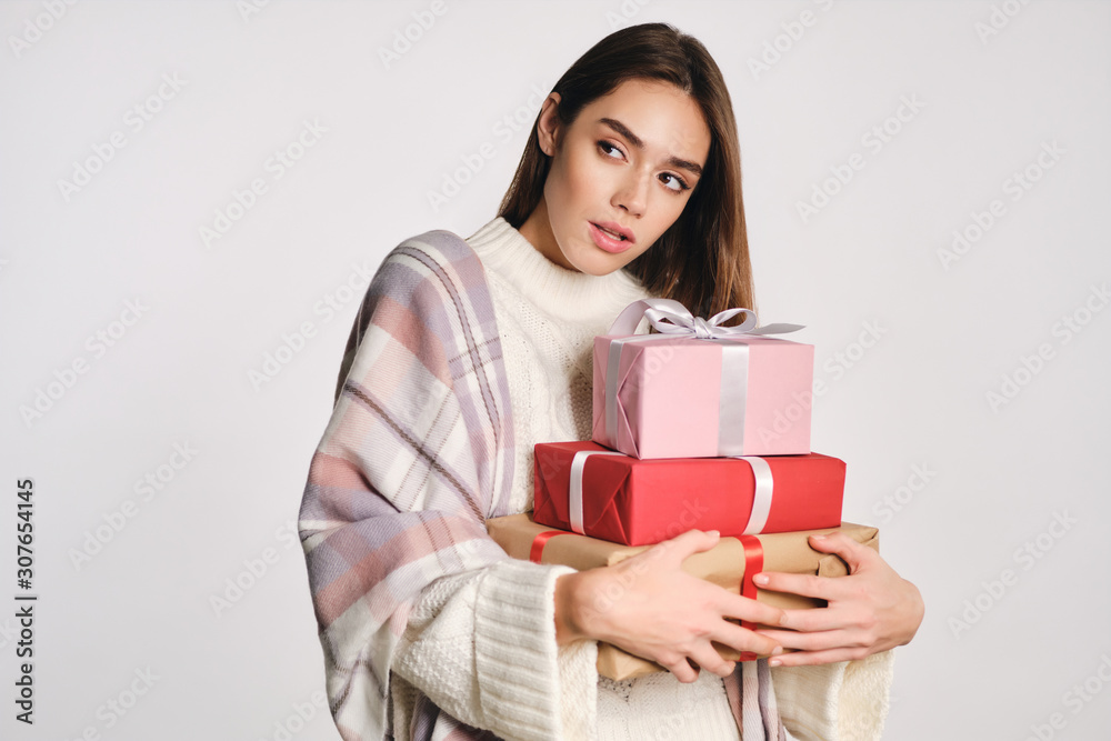 Attractive girl in sweater with plaid on shoulders holding gift boxes thoughtfully looking away over white background Attractive girl in sweater with plaid on shoulders holding gift boxes thoughtfully looking away over white background