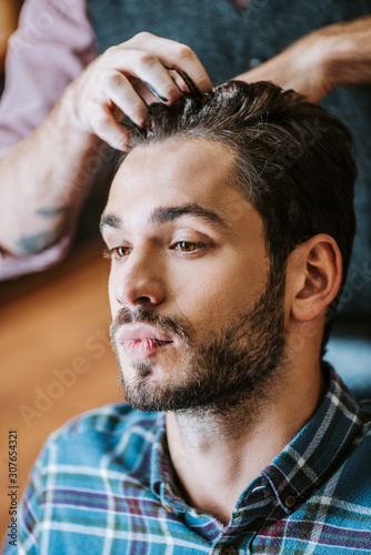 barber with black hair pomade on hands styling hair of handsome man