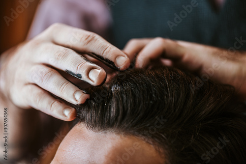 Tableau sur toile cropped view of barber with black hair pomade on hands styling hair of man
