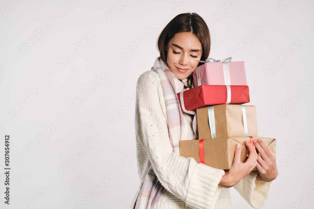 Pretty cute girl in sweater dreamily holding gift boxes in hands over white background Pretty cute girl in sweater dreamily holding gift boxes in hands over white background