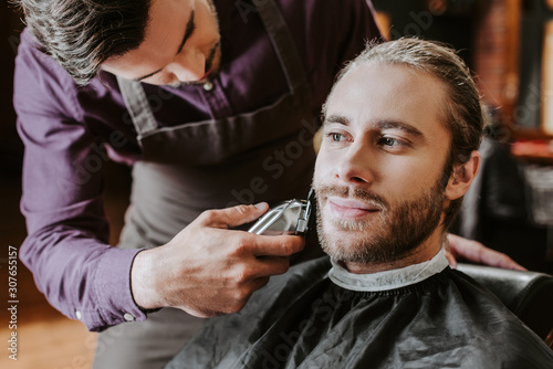 barber holding trimmer while shaving bearded man