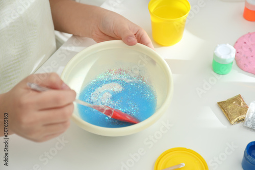 Little girl mixing ingredients with silicone spatula at table  closeup. DIY slime toy