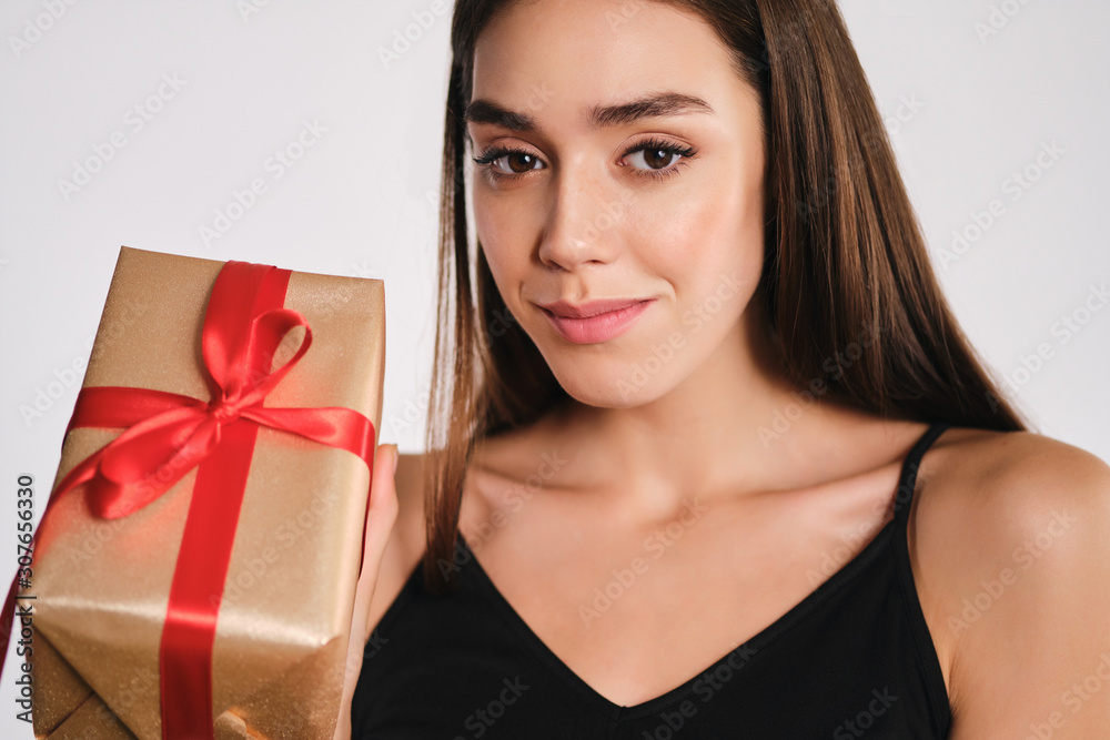 Portrait of attractive smiling girl holding gift box intently looking in camera over white background isolated Portrait of attractive smiling girl holding gift box intently looking in camera over white background isolated