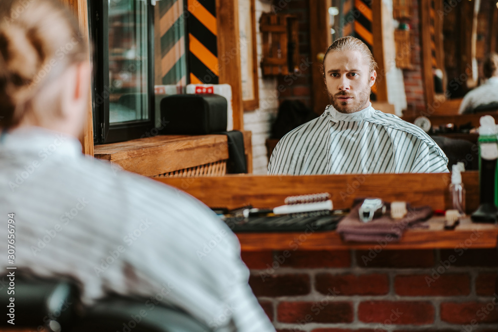 selective focus of handsome bearded man looking at mirror in barbershop