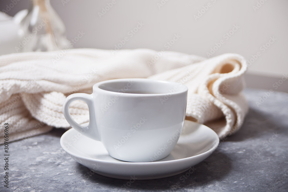 Close up of cup of coffee and knittead white plaid on the gray background Close up of cup of coffee and knittead white plaid on the gray background